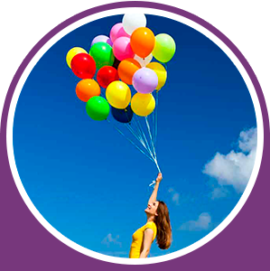 Mujer sosteniendo globos de colores contra un cielo azul brillante.