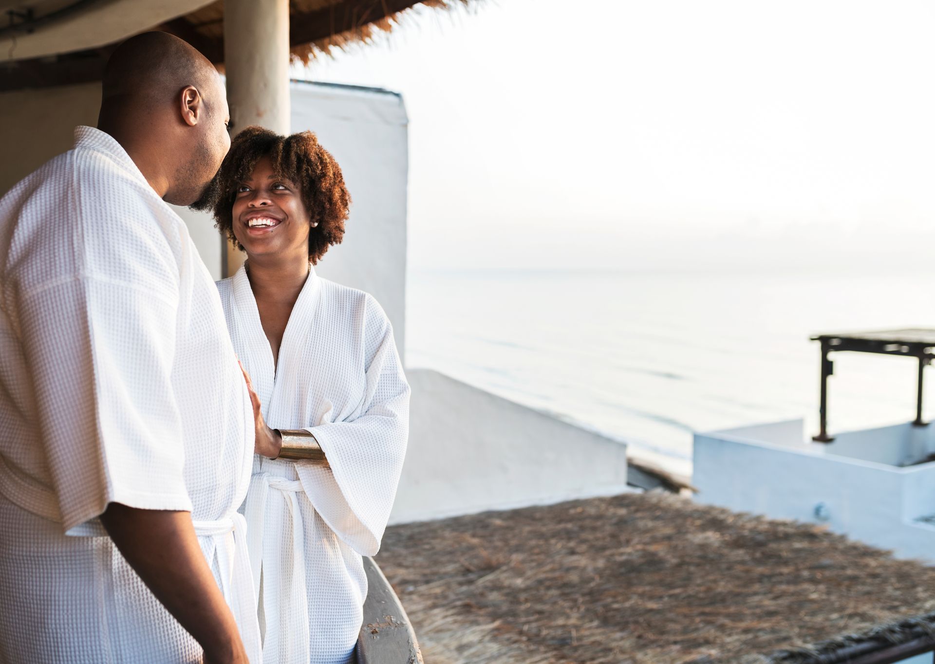 A man and a woman are standing on a balcony overlooking the ocean.