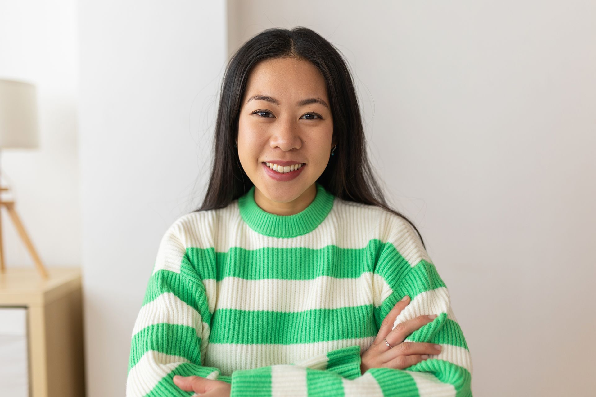 A woman in a green and white striped sweater is smiling with her arms crossed.