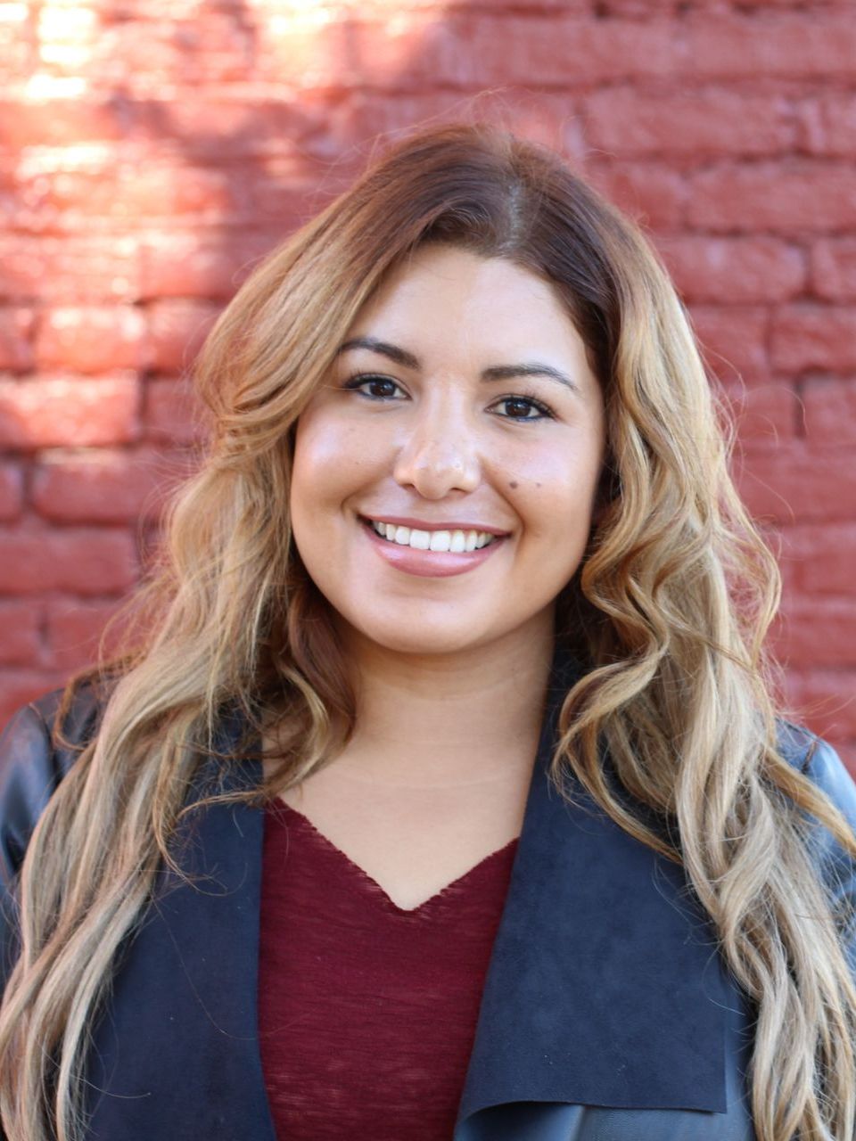 A woman is smiling in front of a red brick wall.