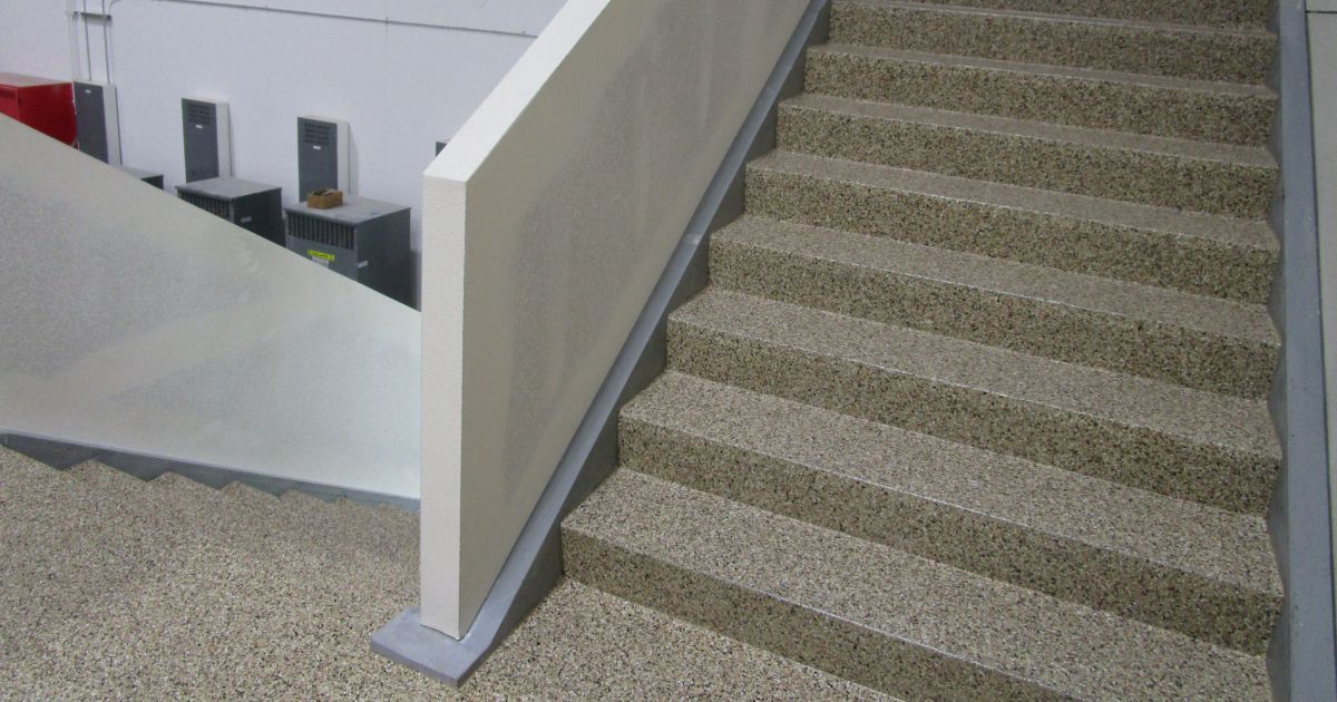Staircase with textured treads and a beige handrail, in an interior setting.