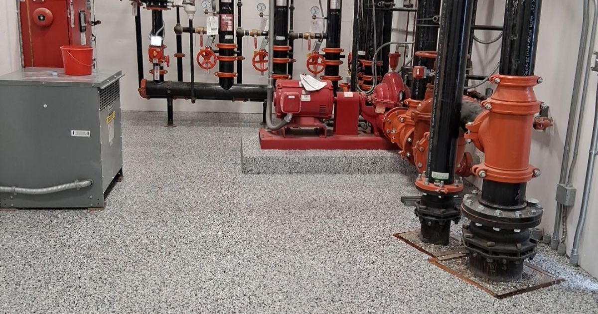Equipment room with fire pumps, piping, and speckled flooring.