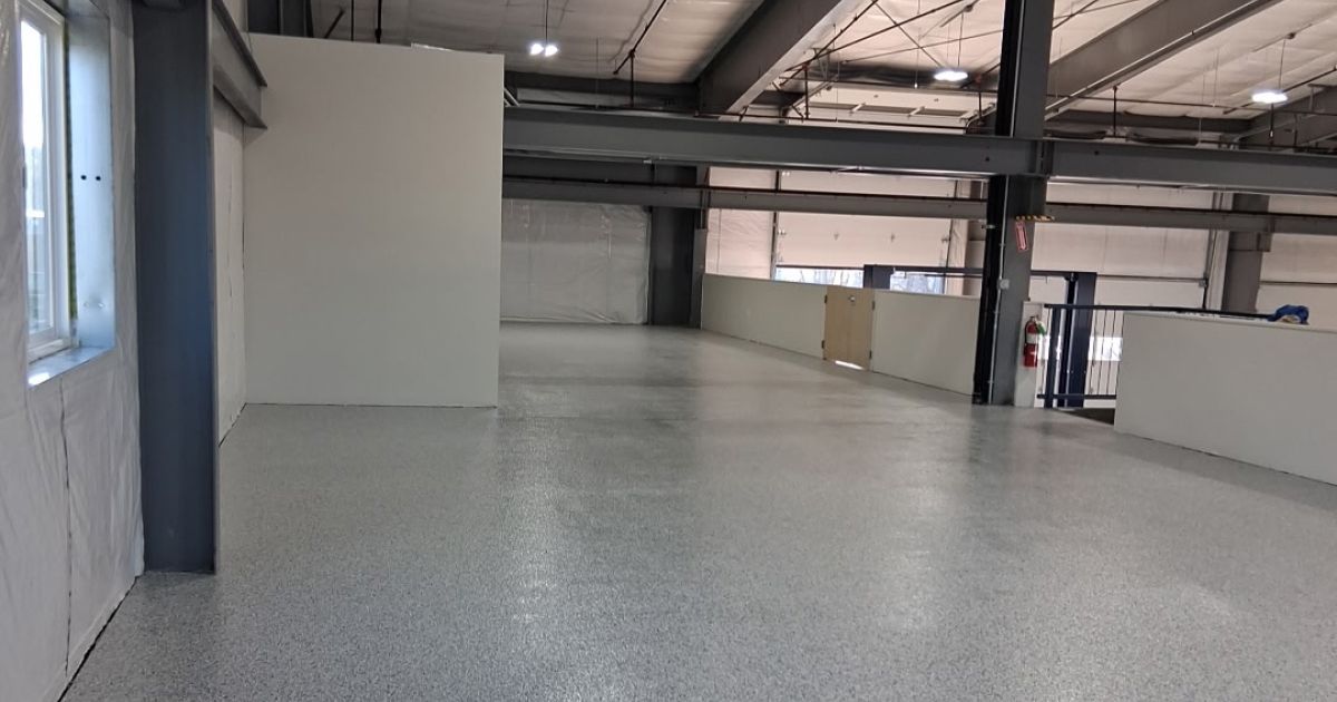 Empty industrial interior with epoxy floor, white walls, and exposed metal beams.