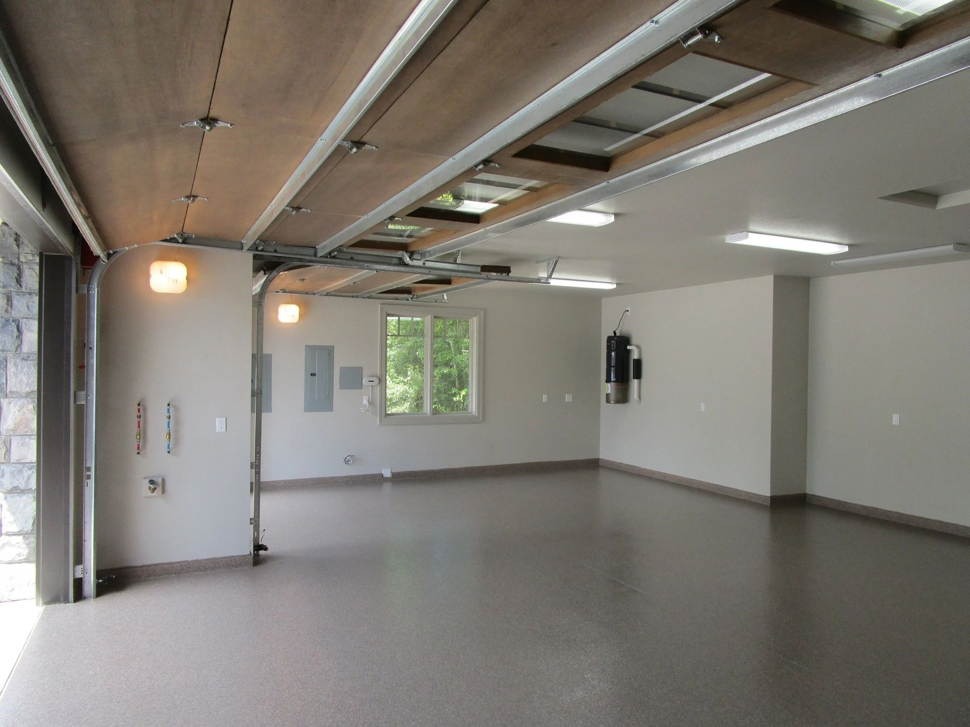 Empty, clean garage with a gray epoxy floor and white walls. Garage door is open.