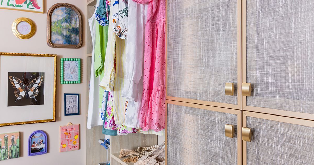 A closet with hanging clothes in bright colors next to cabinets with gold hardware and artwork on the wall.