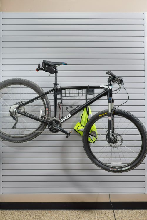 Black mountain bike hanging on a gray slat wall in a garage. Yellow vest hangs from the bike.