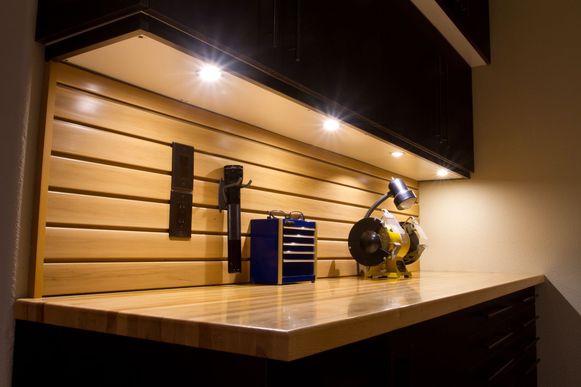 Workshop with wooden pegboard wall and tools, illuminated by overhead lights.