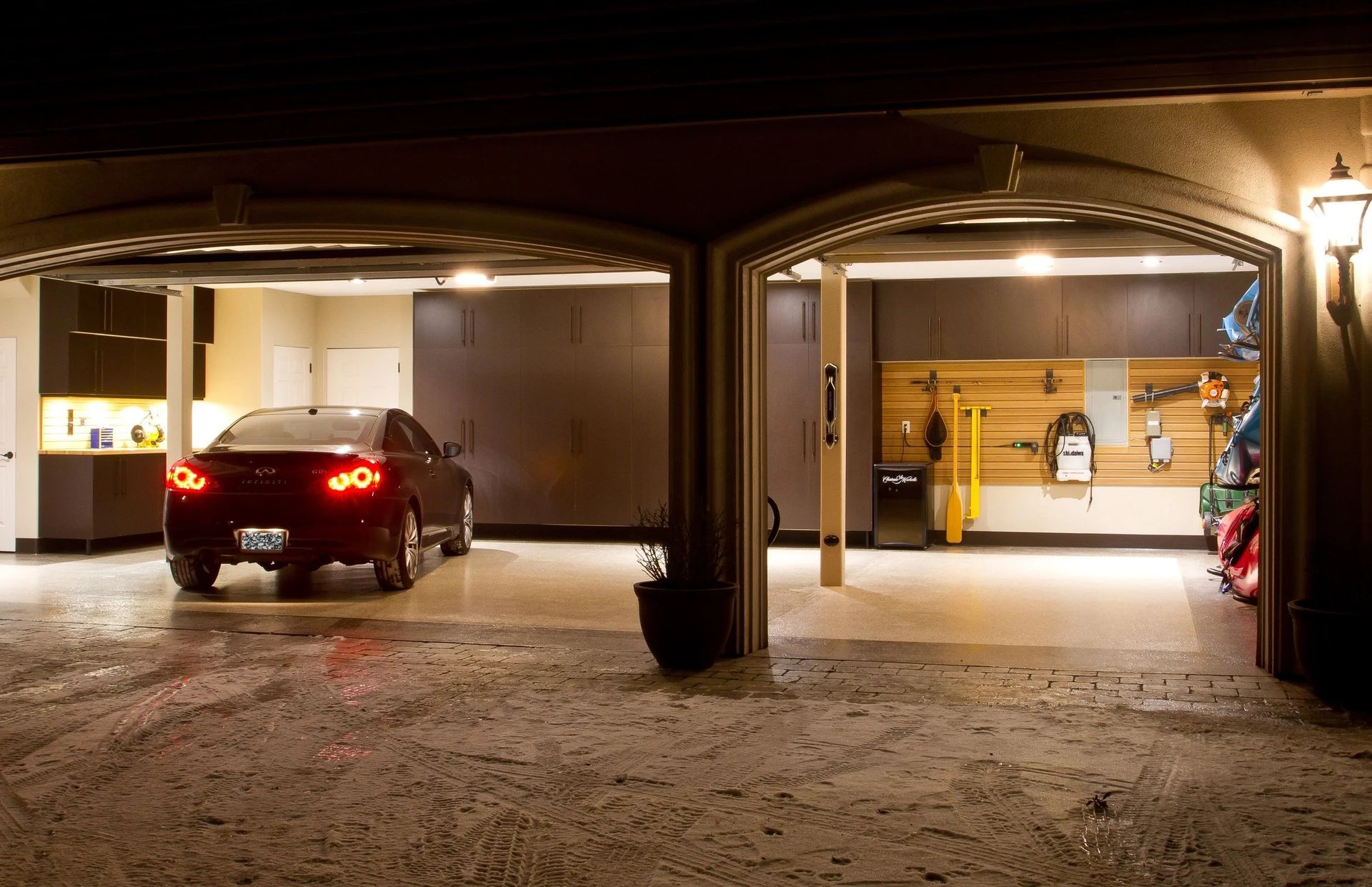 A car parked in a well-lit two-car garage at night. Tools and storage visible on the right.