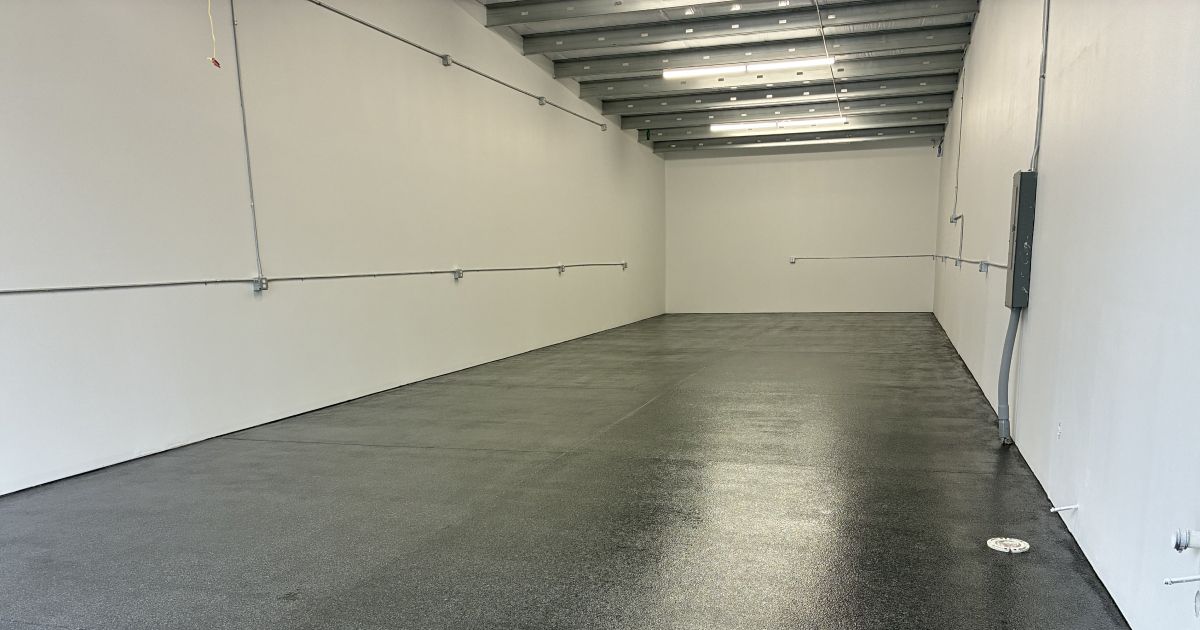 Empty room with white walls, a dark floor, and exposed ceiling beams.