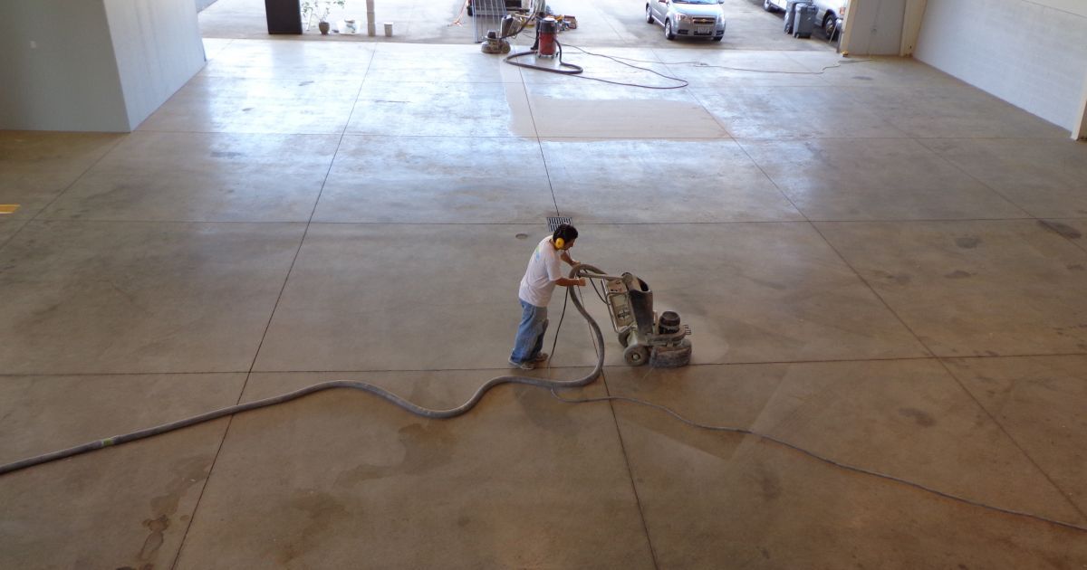 Person using concrete grinding machine on a large concrete floor, outdoors.