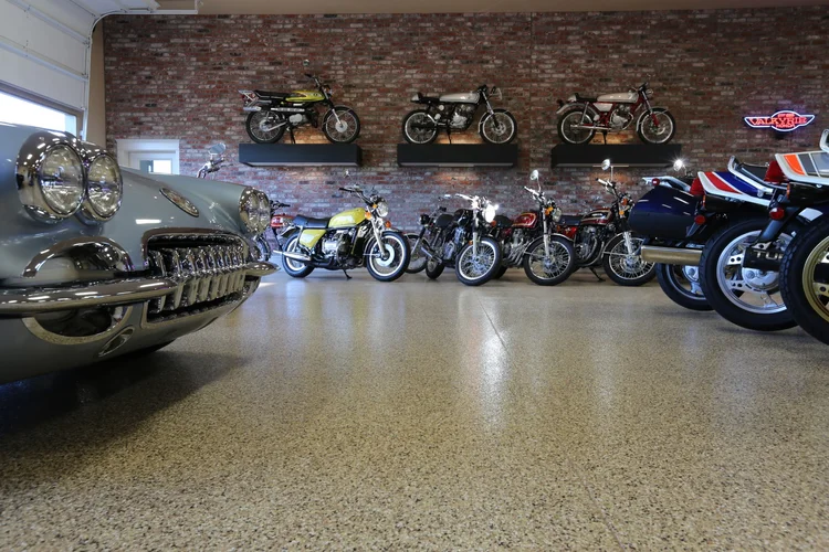 Classic cars and motorcycles displayed in a showroom with brick wall and polished floor.