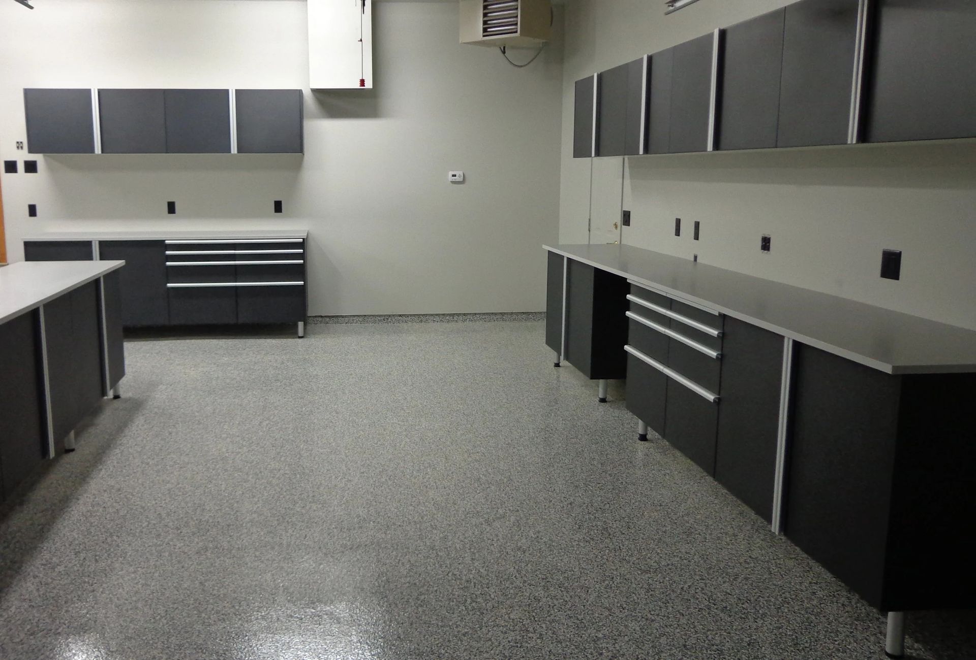 Garage interior with grey cabinets, countertops, and speckled flooring. Empty.