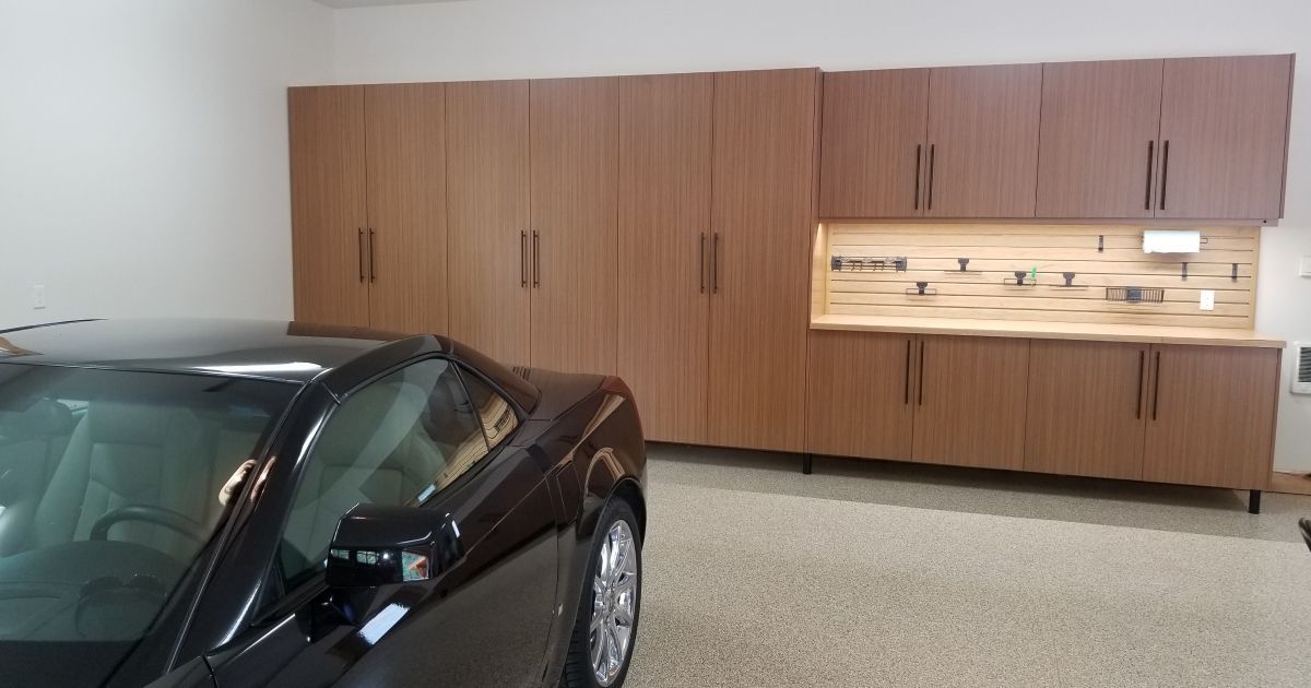 Black car in a garage with wood storage cabinets along the wall.