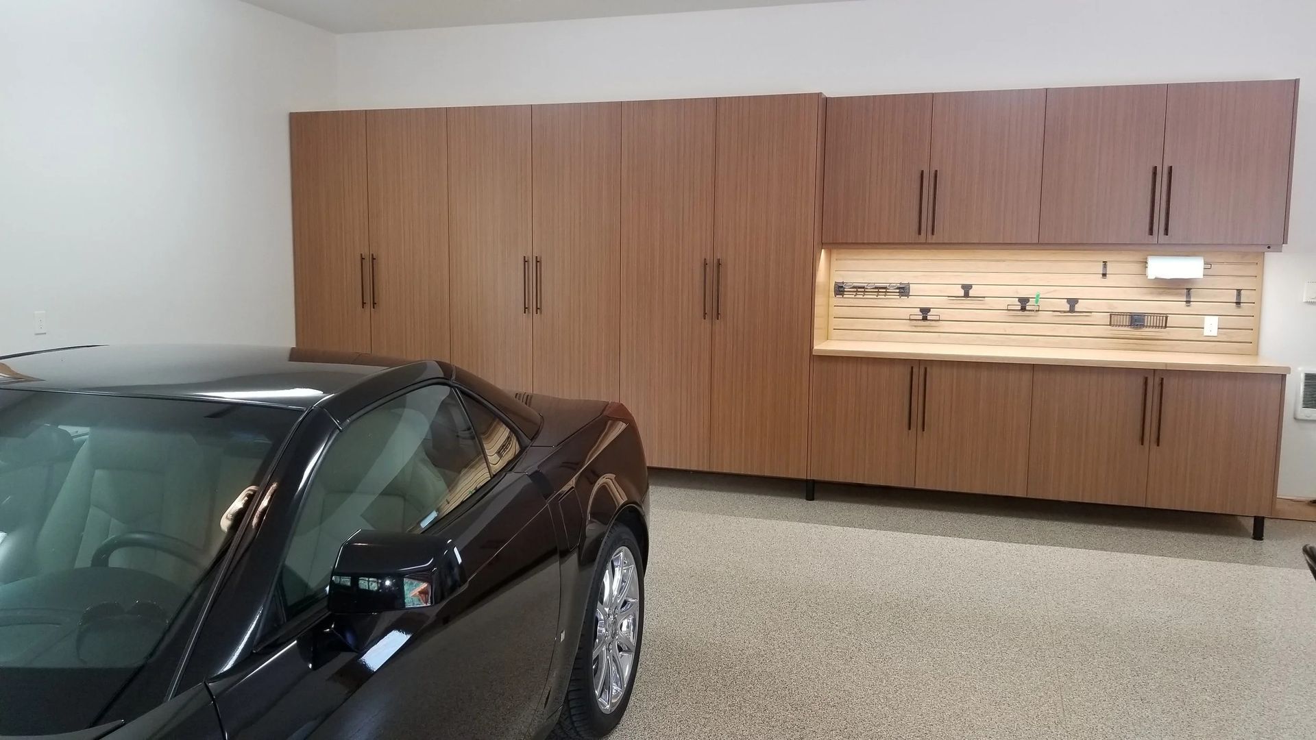Black sports car parked in front of wooden garage cabinets with a workbench.
