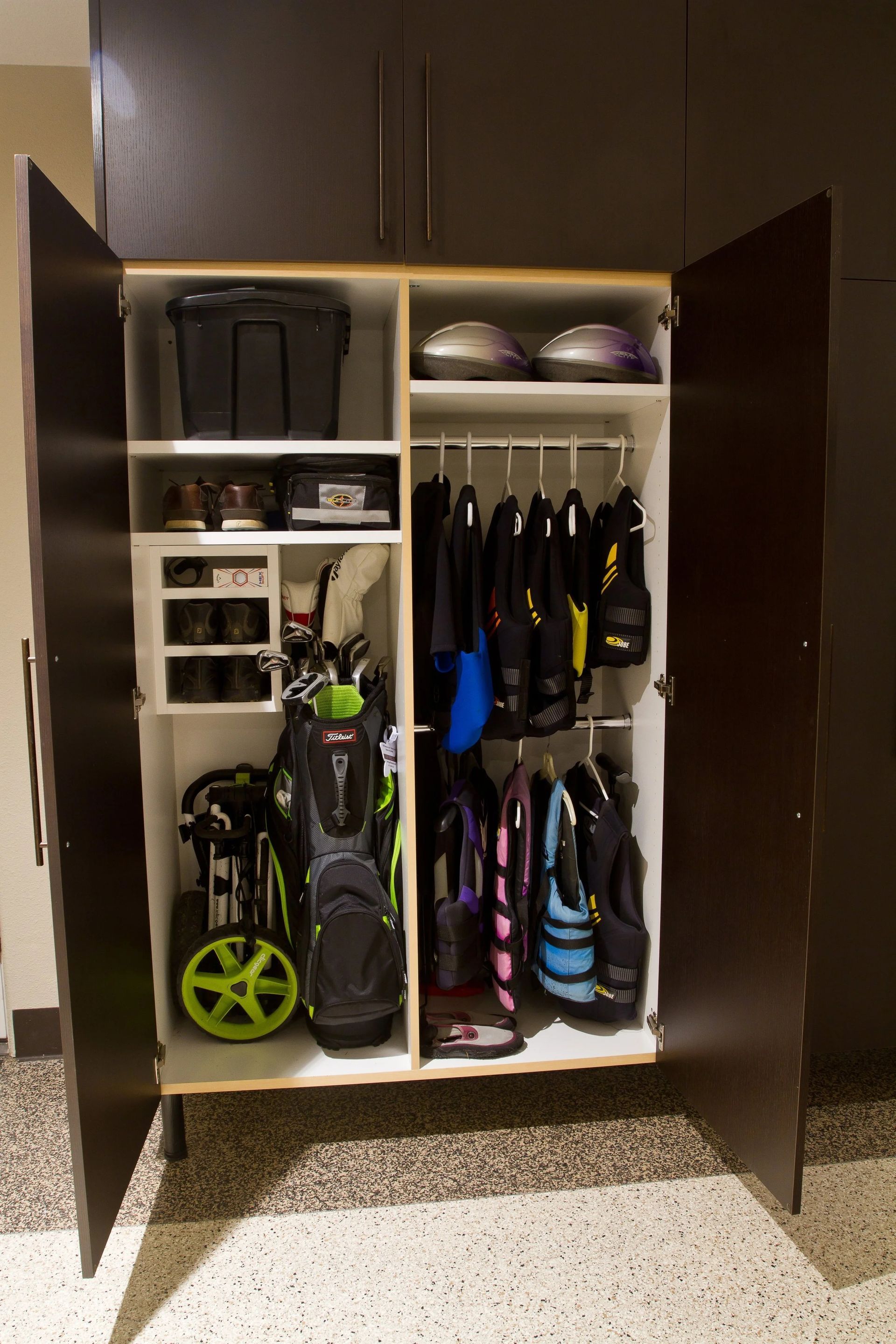 Storage cabinet filled with golf bags, shoes, helmets, and other equipment; inside a garage.