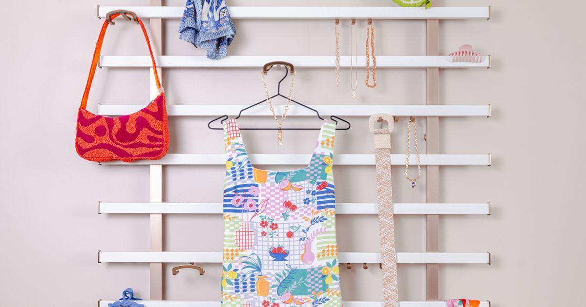 White wall-mounted clothing rack with items: orange bag, dress, jewelry, and accessories.