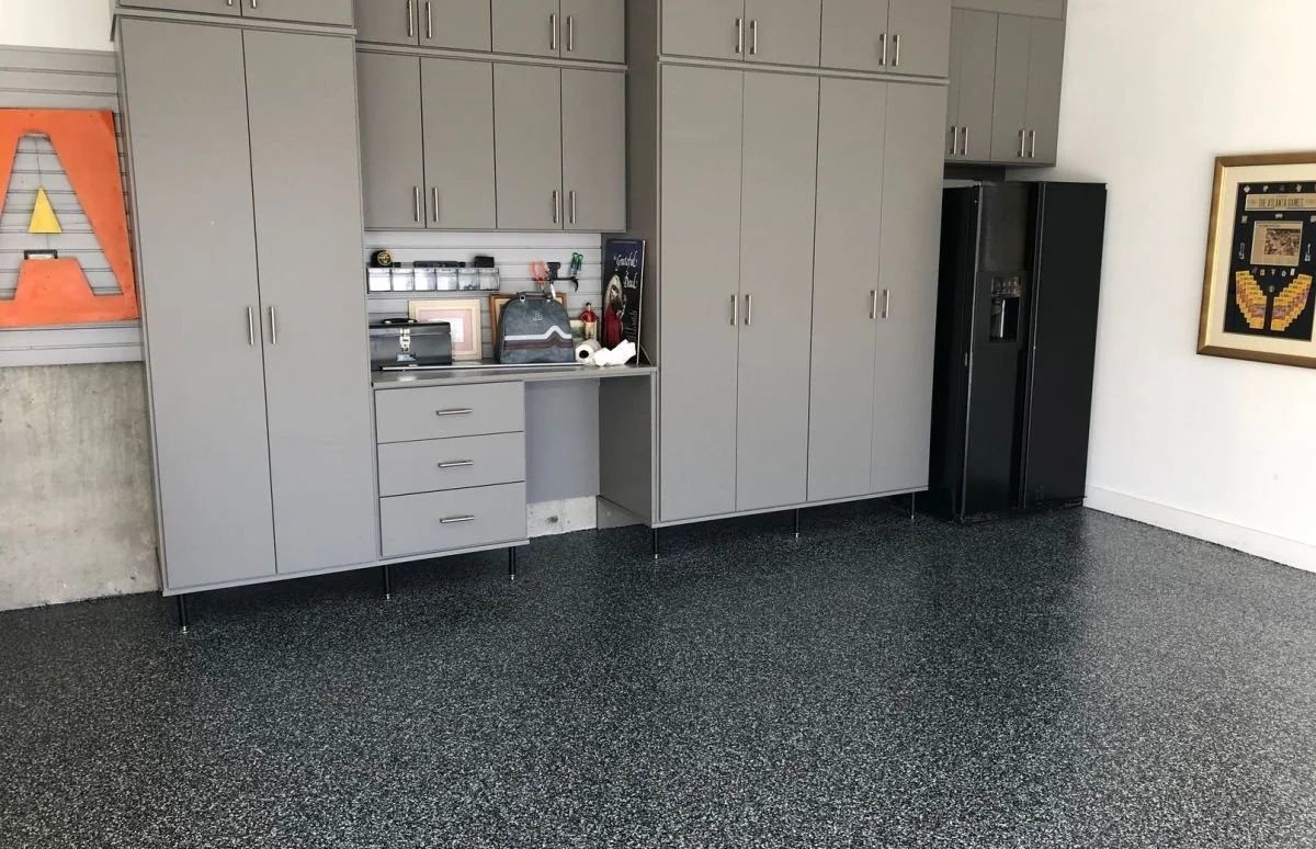 Garage with gray cabinets, black appliances, speckled floor, and artwork.