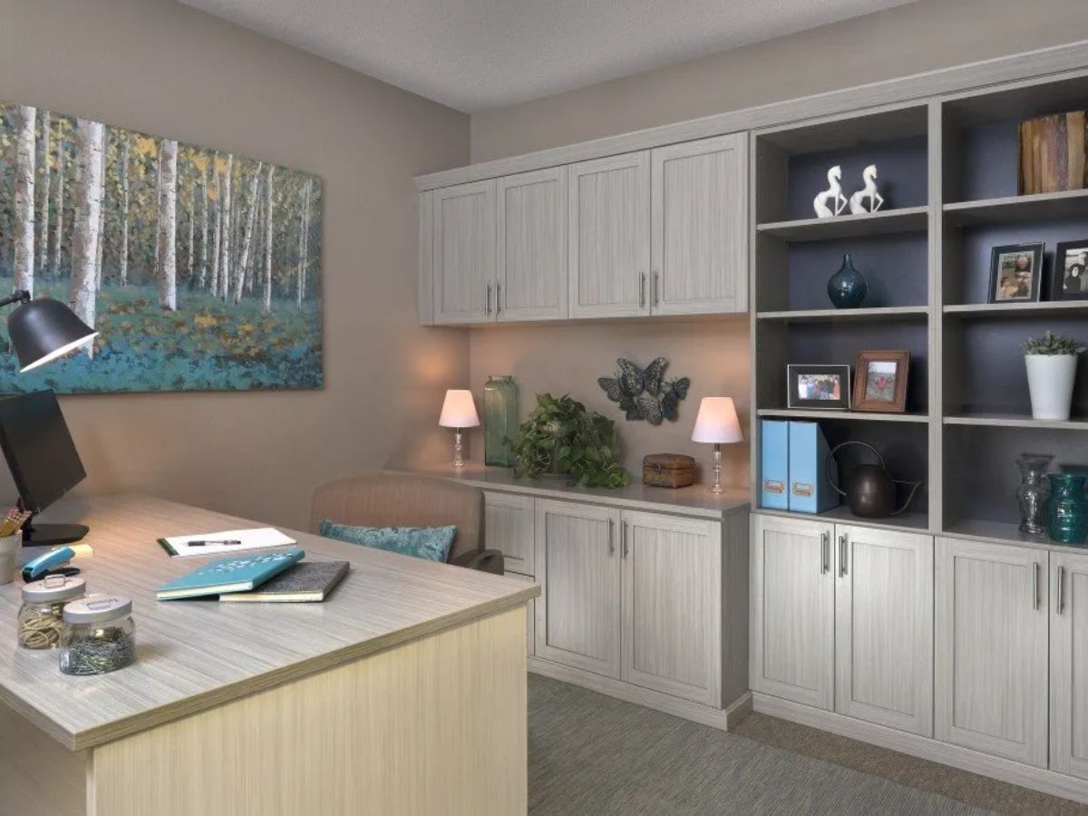 A home office with a desk , shelves , and a painting on the wall.