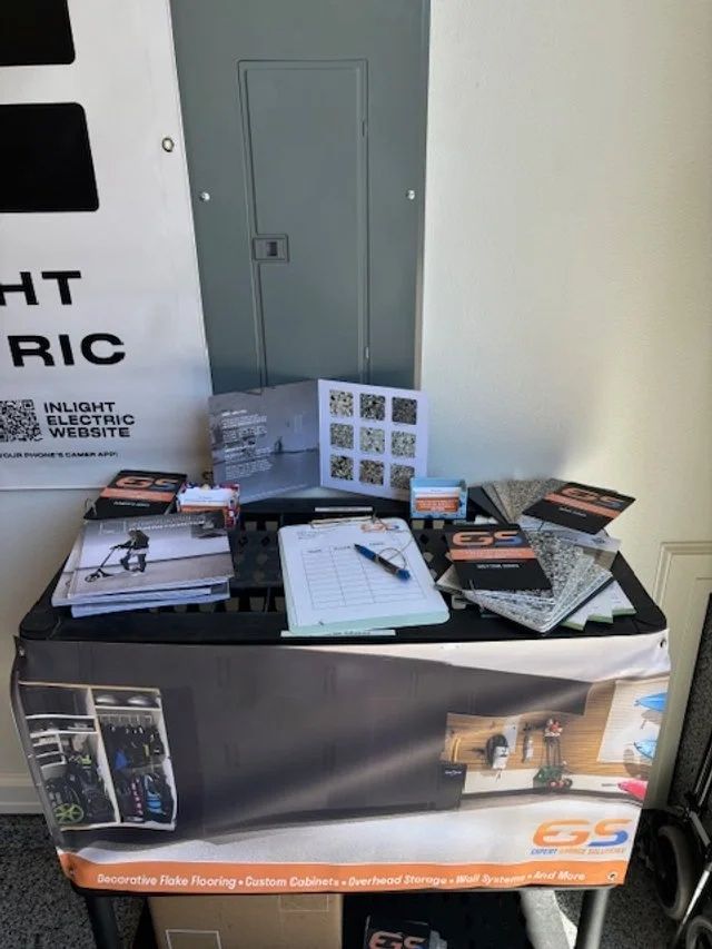 Table with brochures, sign-up sheet, and QR codes; electrical panel in the background.