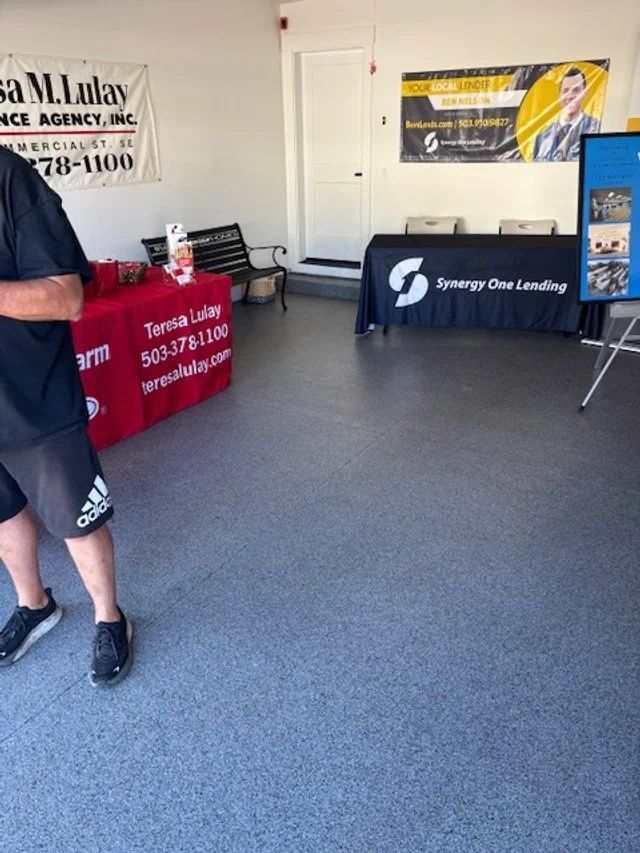 Person stands near tables at an event. Tables have company banners and a bench is behind them.