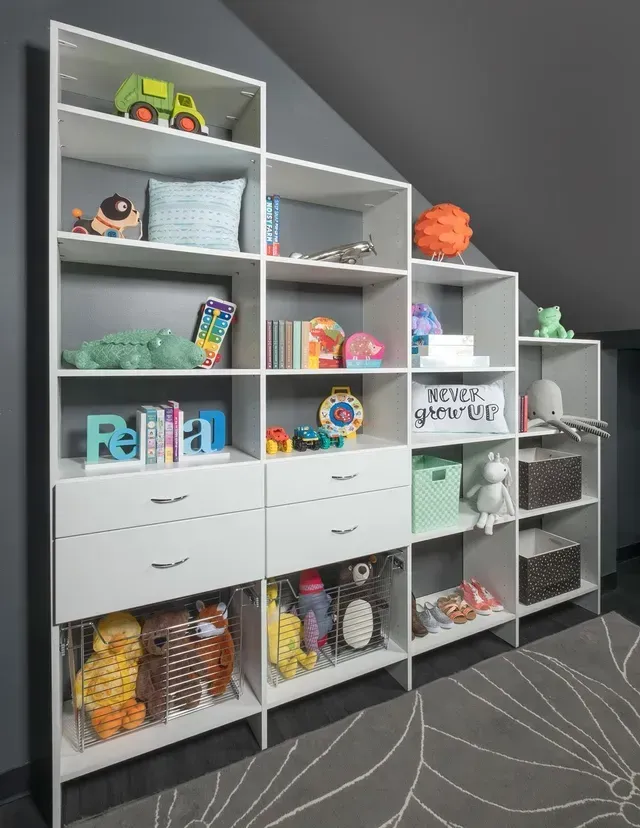 White shelves with toys in a gray-walled room. Angled design follows the wall's slope.