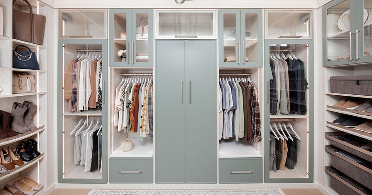 Walk-in closet with pale blue cabinets, rods of clothes, and shelves for shoes and accessories.
