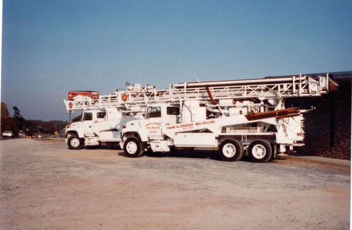 Two white trucks are parked next to each other on a dirt road