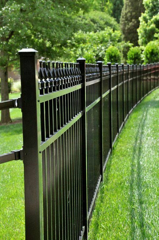 A black metal fence surrounds a gravel path in a yard.
