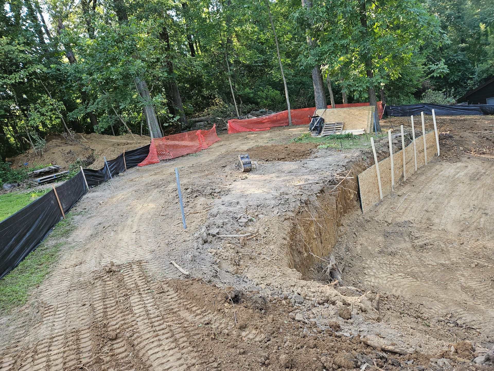 Dirt construction site with erosion control fencing and stakes in front of a forest.