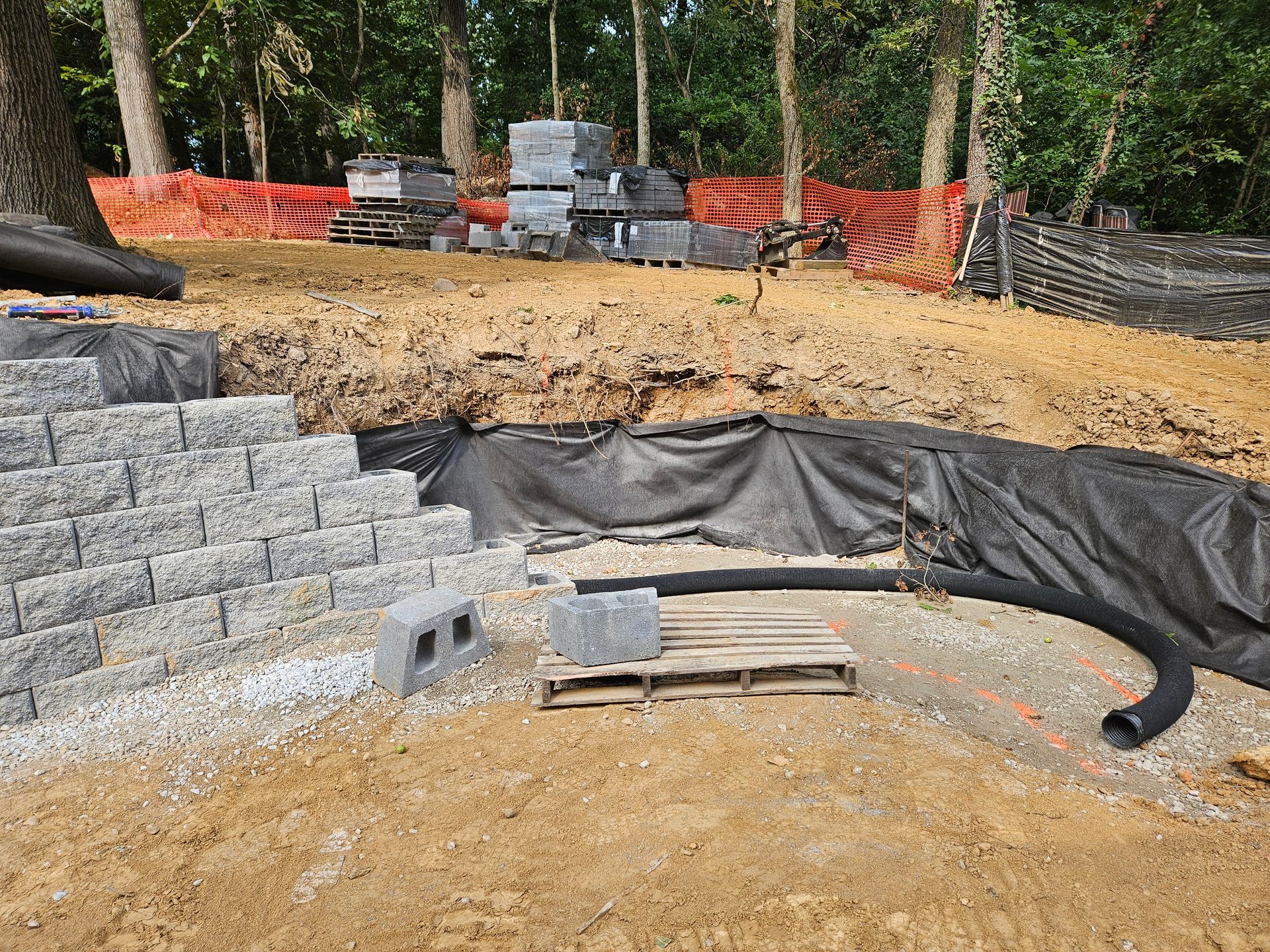 Construction site with retaining wall being built with gray stone blocks and landscaping fabric.