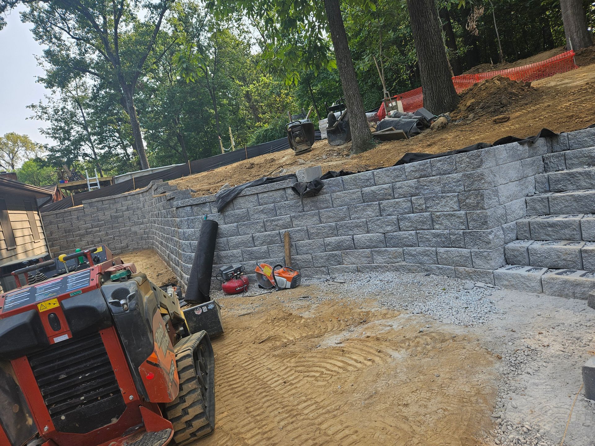 Construction site with retaining wall made of gray blocks, steps, and machinery.