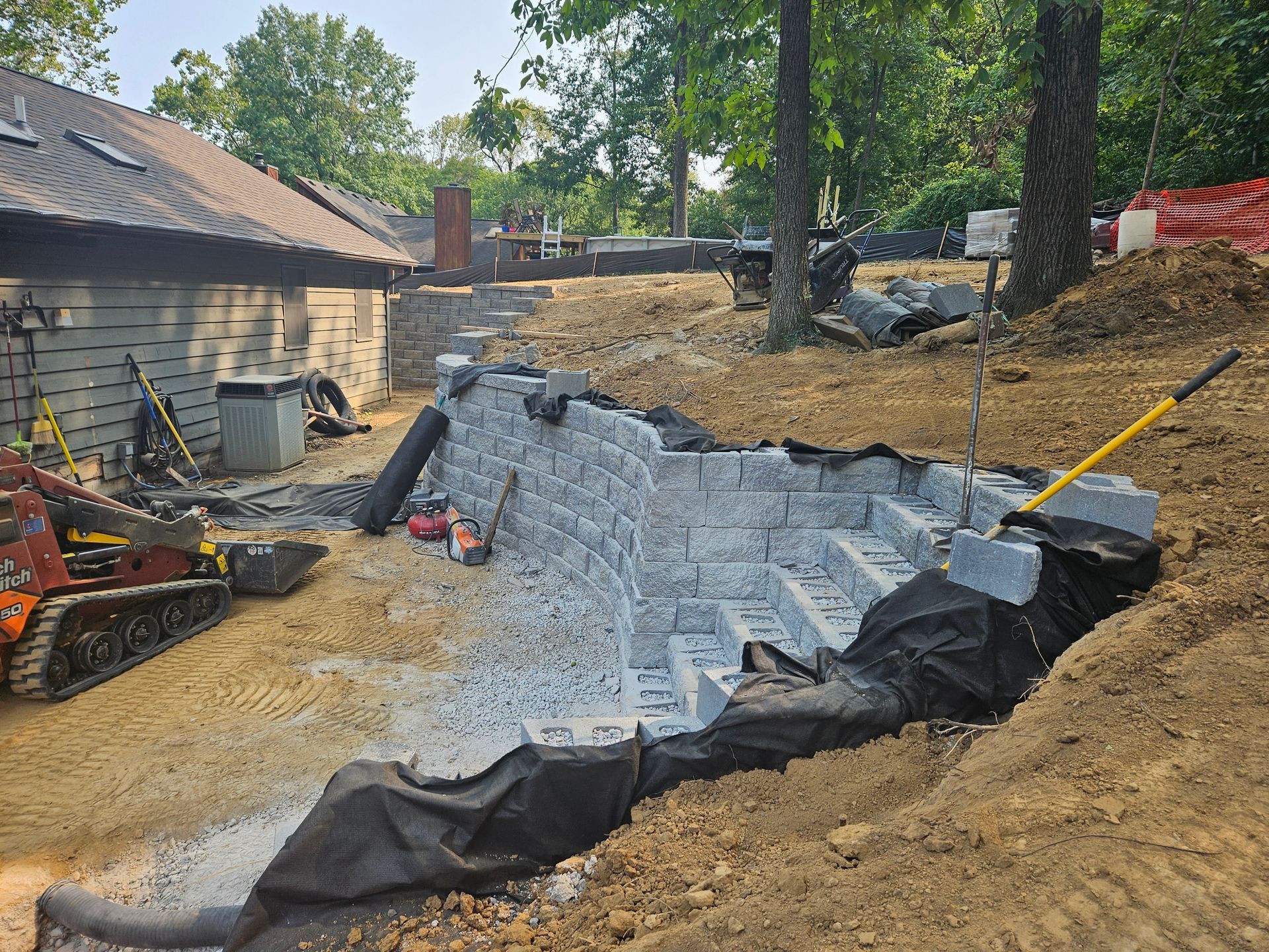 Construction site: stone steps being built into a hillside, with a small excavator, and a building in the background.