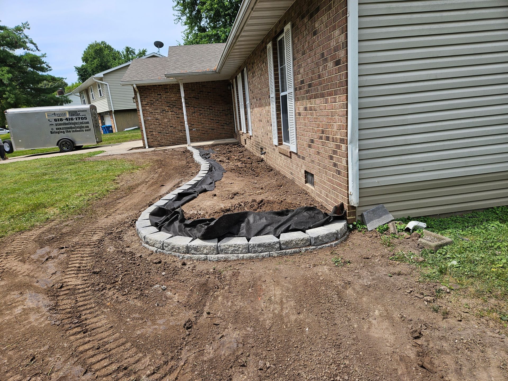 A newly constructed flower bed with a retaining wall next to a brick house. Soil and landscape fabric are visible.