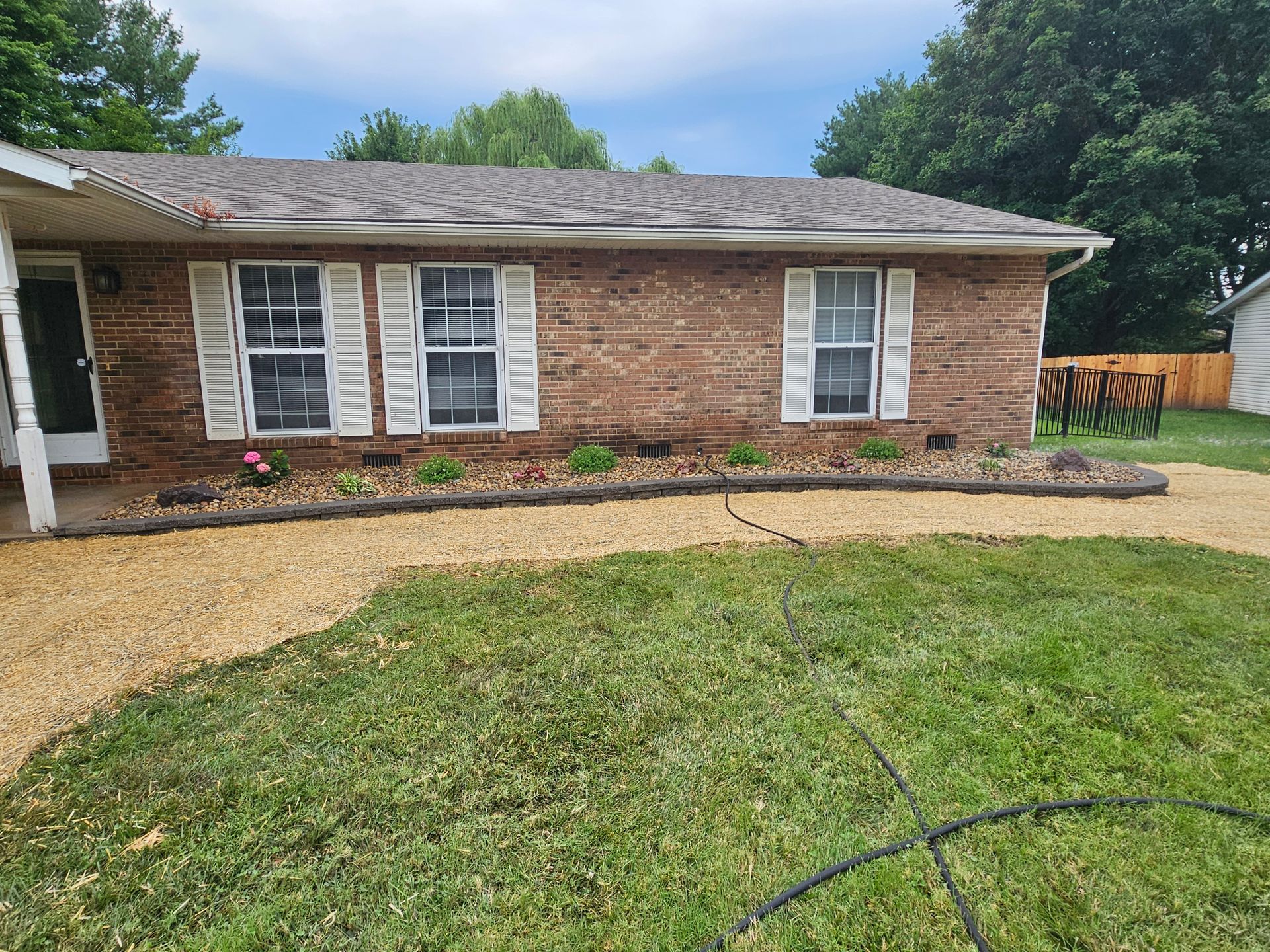 Brick house with white shutters, gravel pathway, and a grassy front yard.