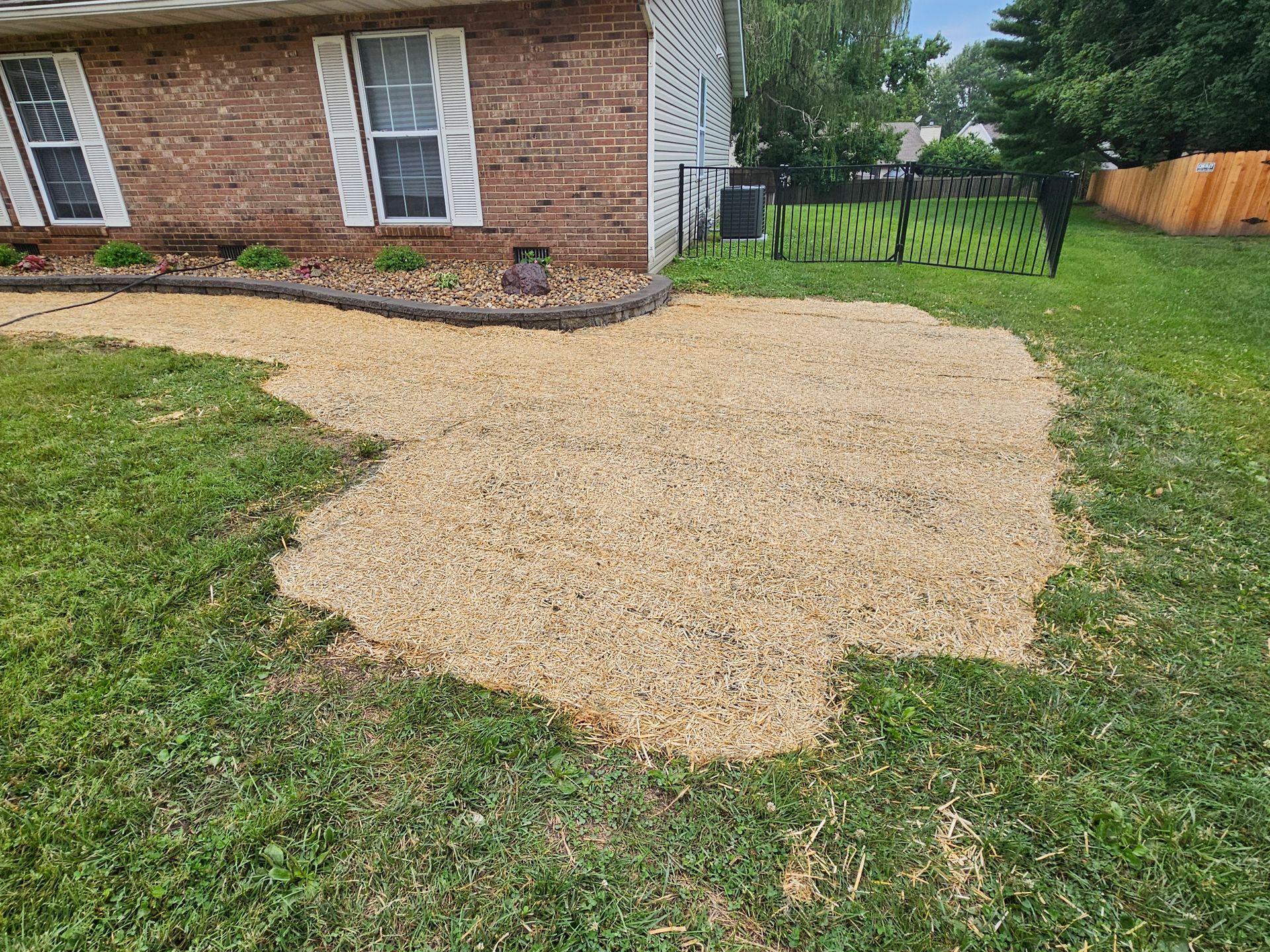 Gravel patio next to a brick house with a flower bed border and adjacent green grass.