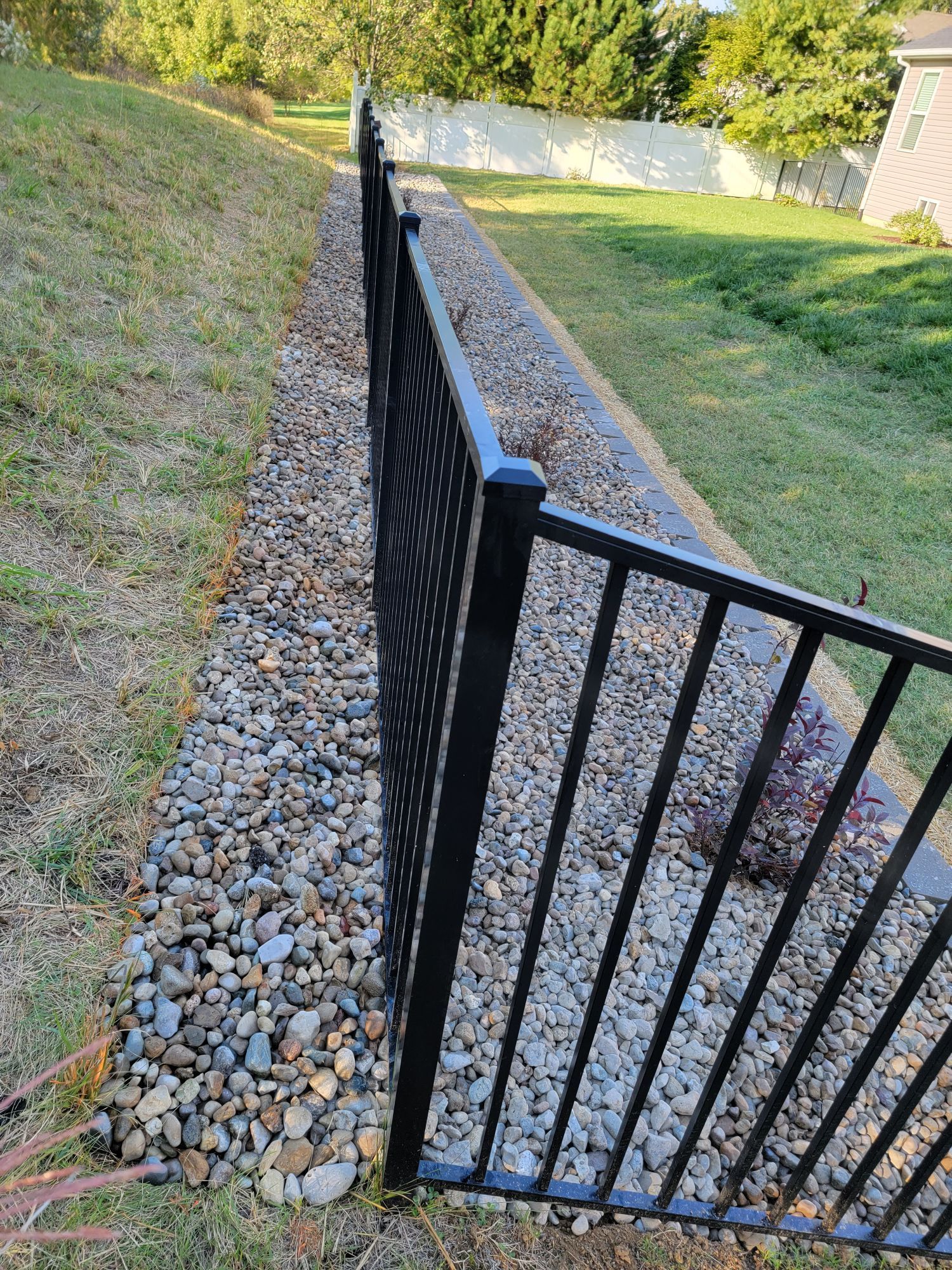 A black metal fence surrounds a gravel path in a yard.