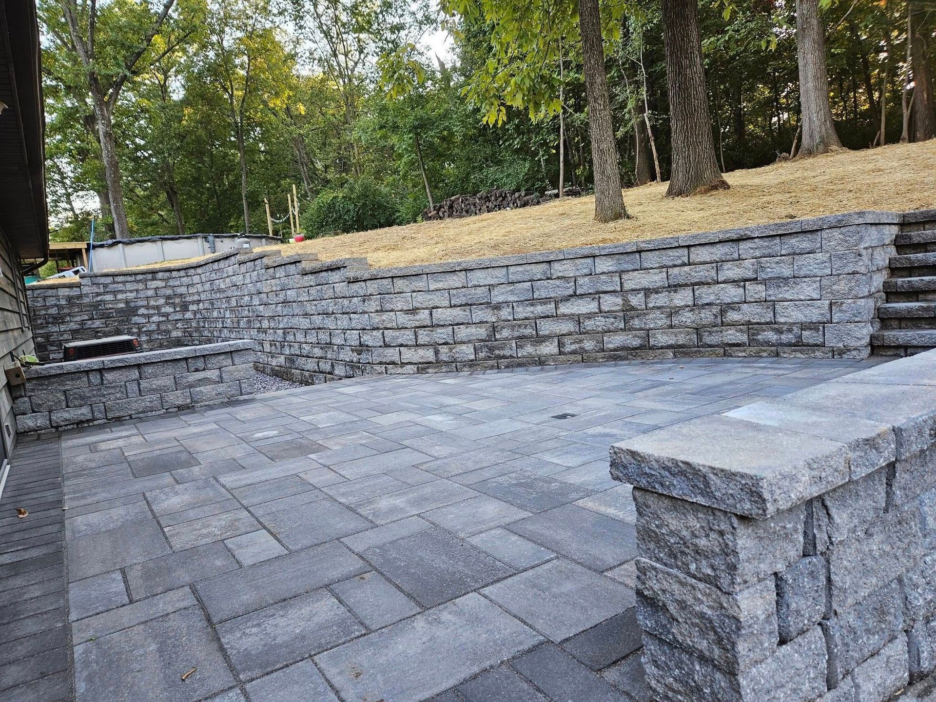 A patio with a stone wall and stairs surrounded by trees.