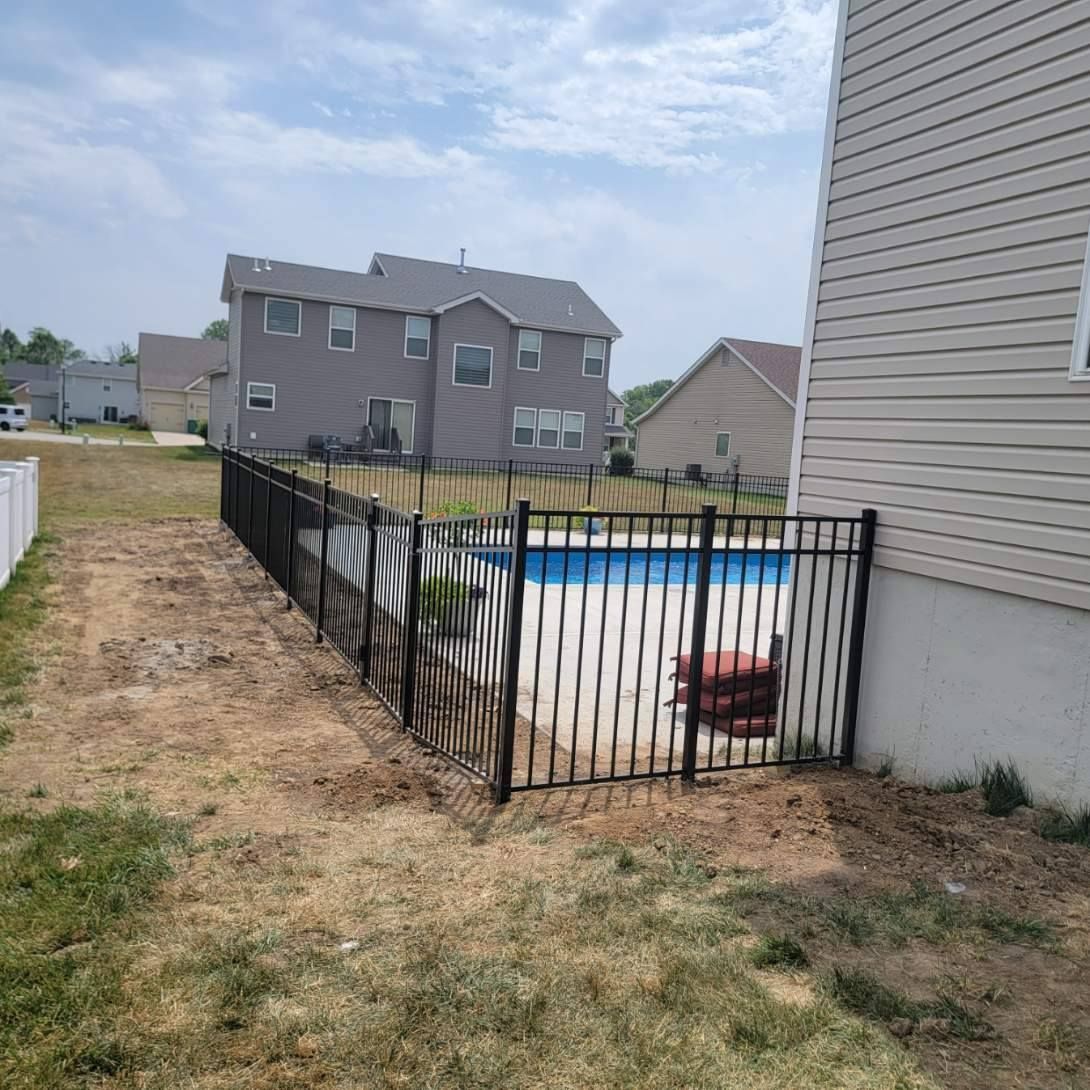 A fence surrounds a swimming pool in front of a house.