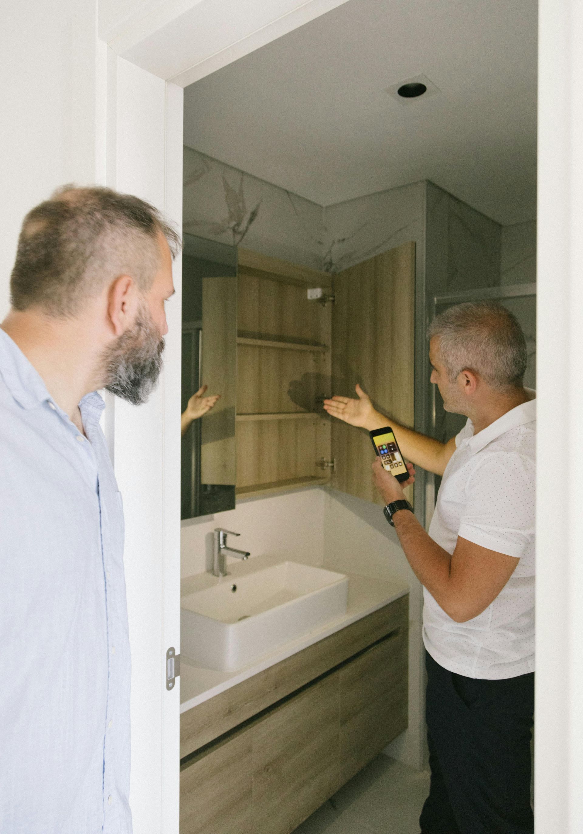 Two men are standing in a bathroom looking at a sink.