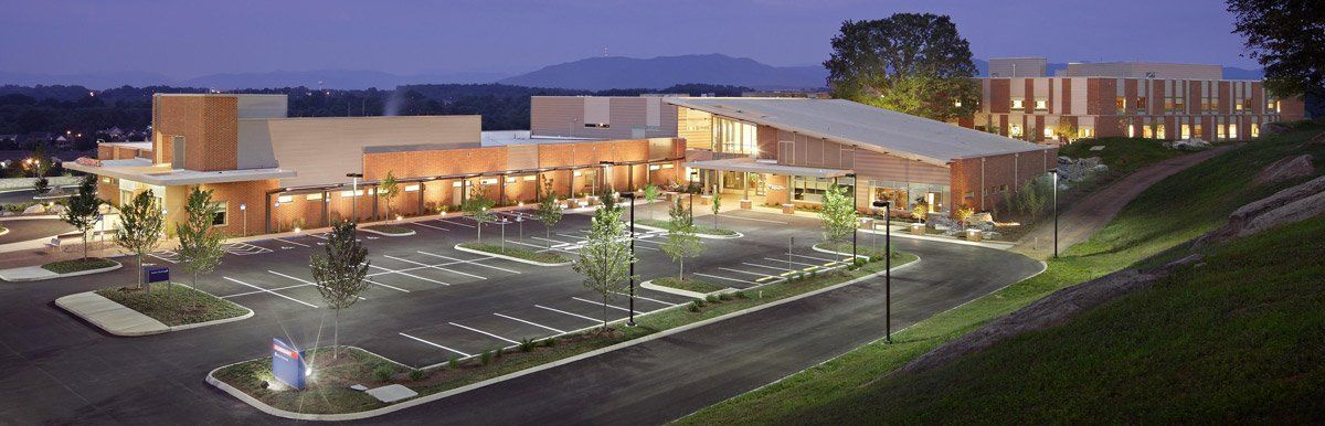 A large building with a parking lot in front of it is lit up at night.