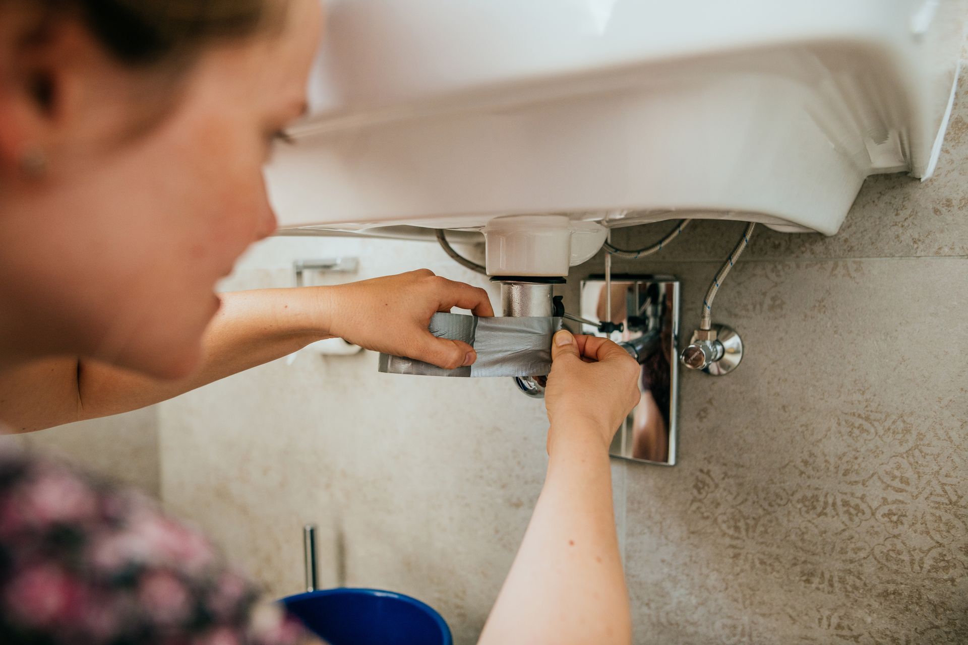 Woman trying to fix a leak in a sink using strong tape. Woman trying to fix a leak in a sink using strong tape.
