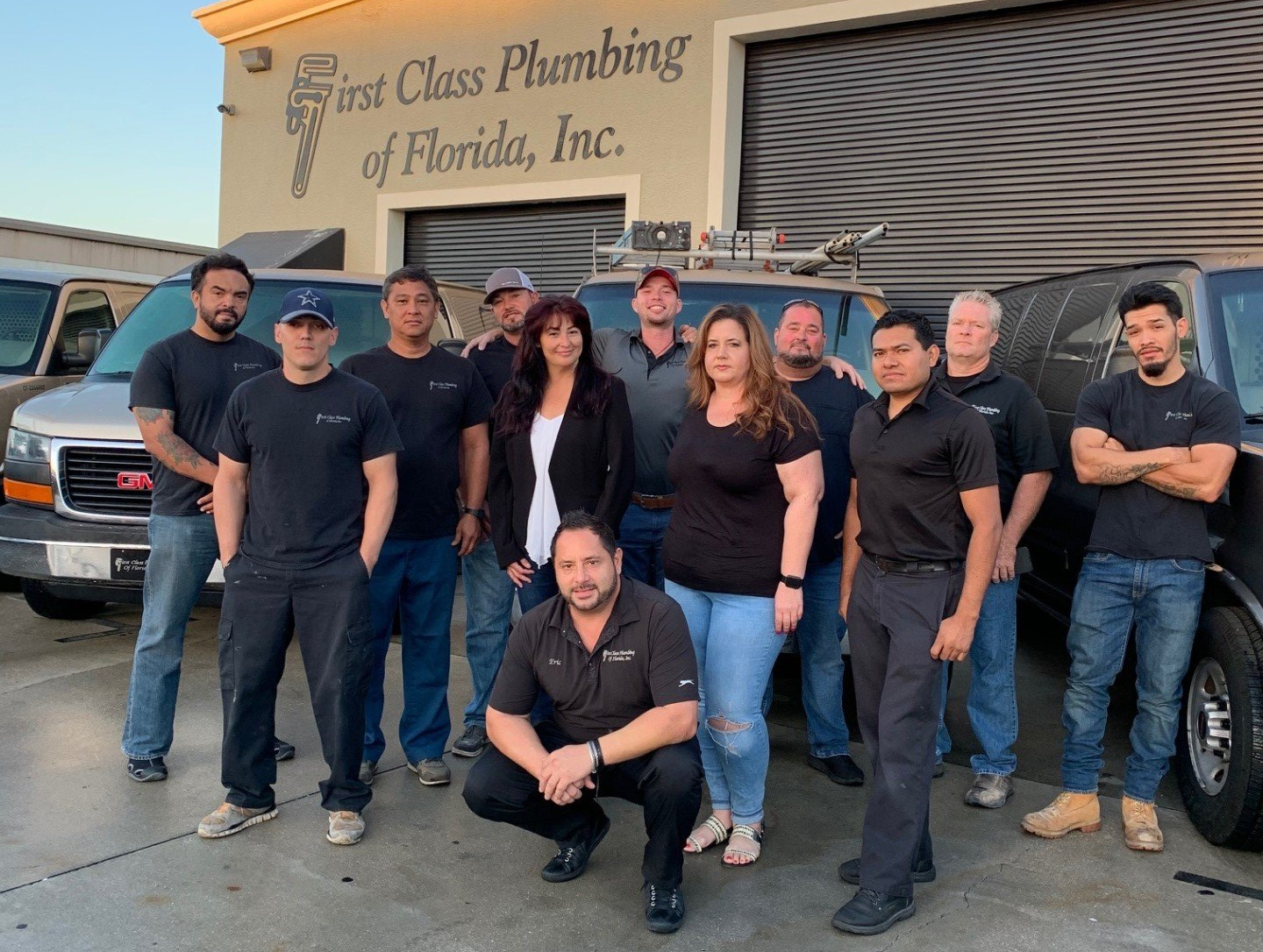 Team of plumbers posing in front of their vans outside a building.