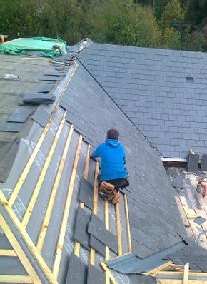  Roofer replacing slate tiles on slanted roof of domestic property