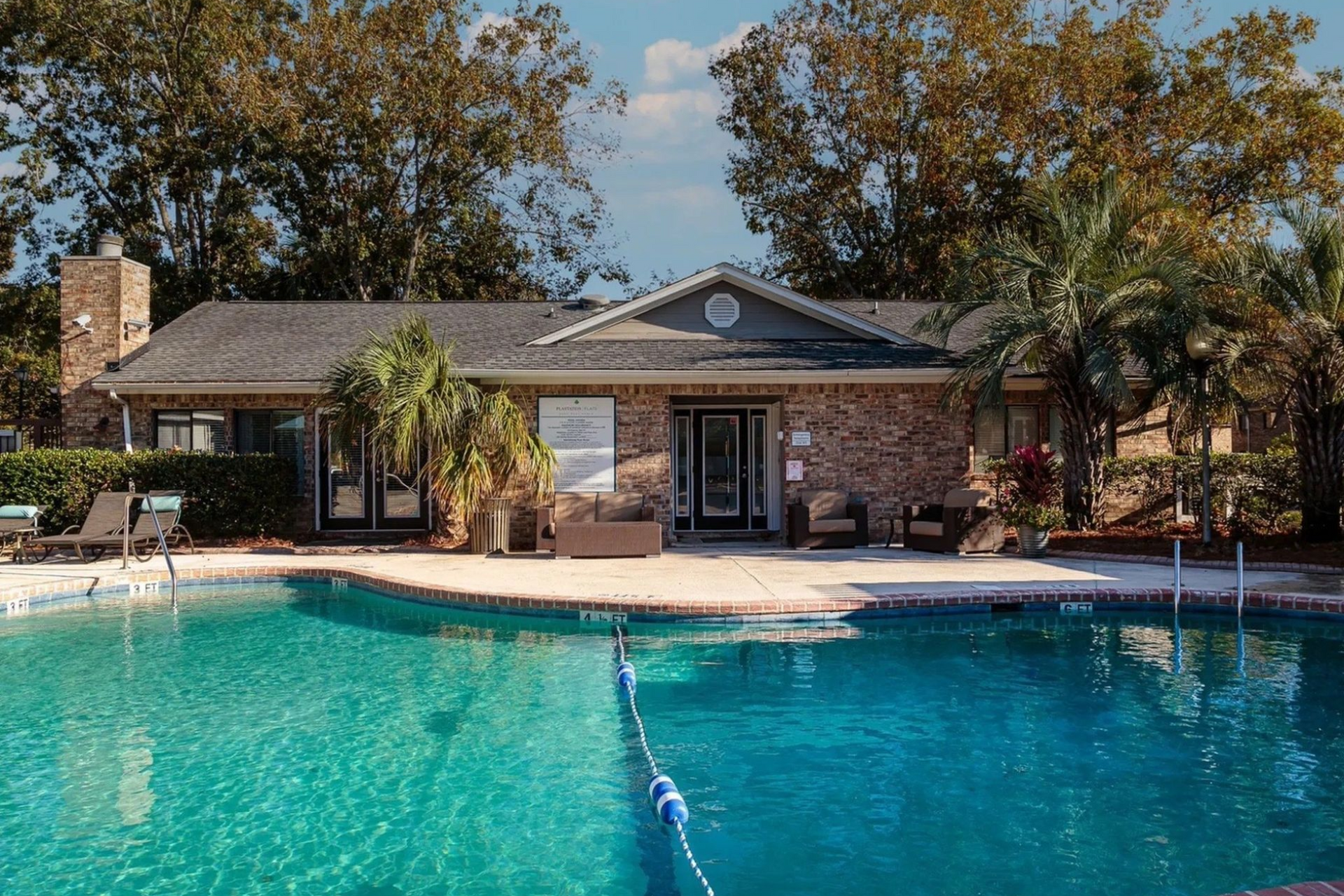 Swimming pool area with lounge chairs and brick building in background.