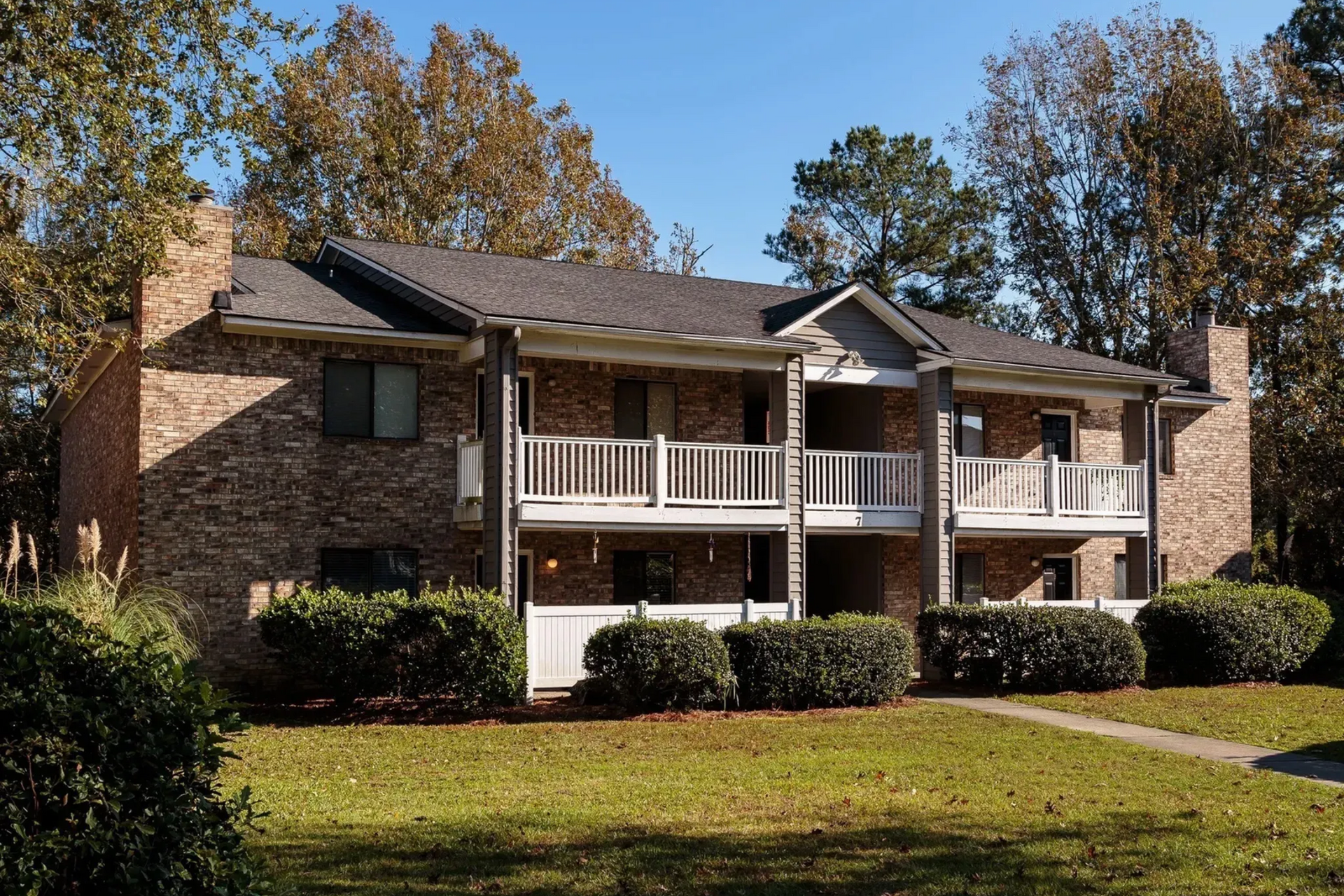 Exterior view of a brick apartment building with balconies and green landscaping.