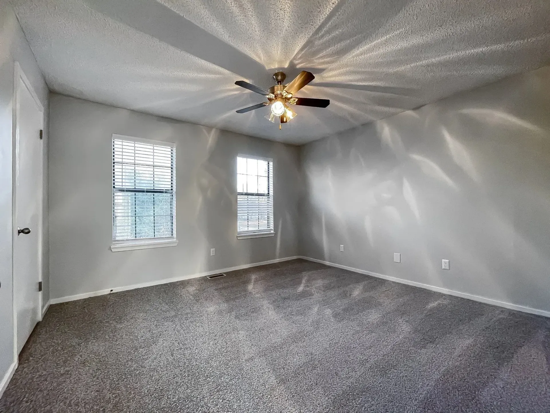 A vacant apartment room with two windows and a ceiling fan.