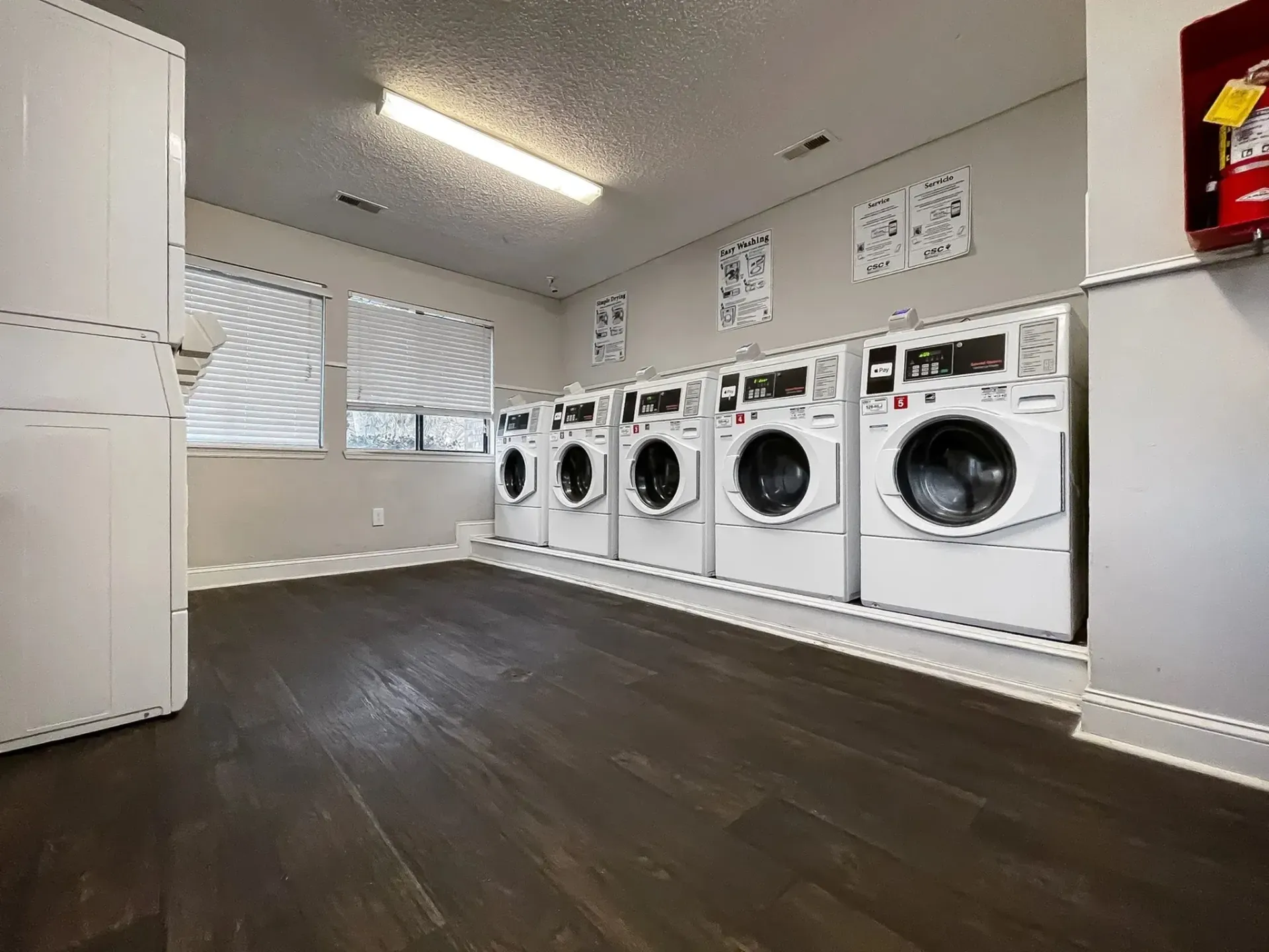 Laundry room with row of washing machines and dryer, natural light from windows