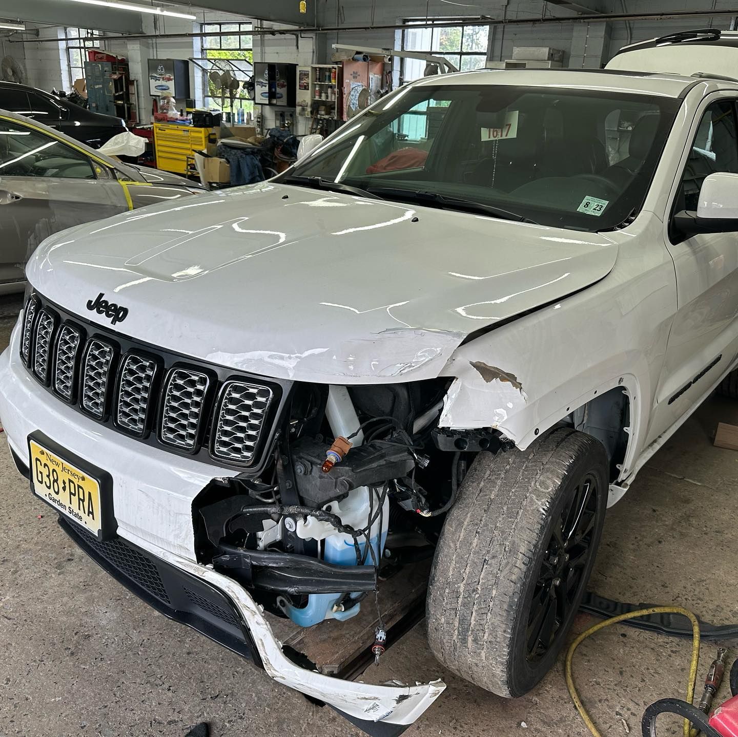 White Jeep SUV with significant front-end damage in a repair shop.