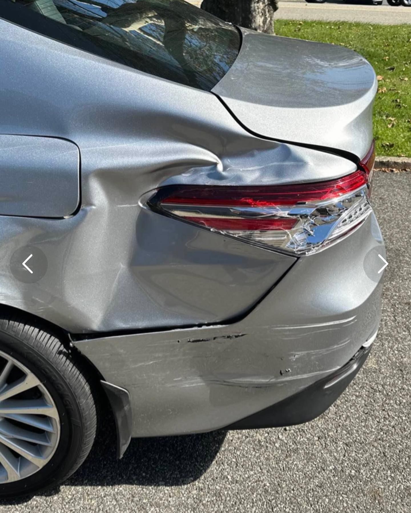 Damaged silver car rear quarter panel; dented, near taillight, and bumper.
