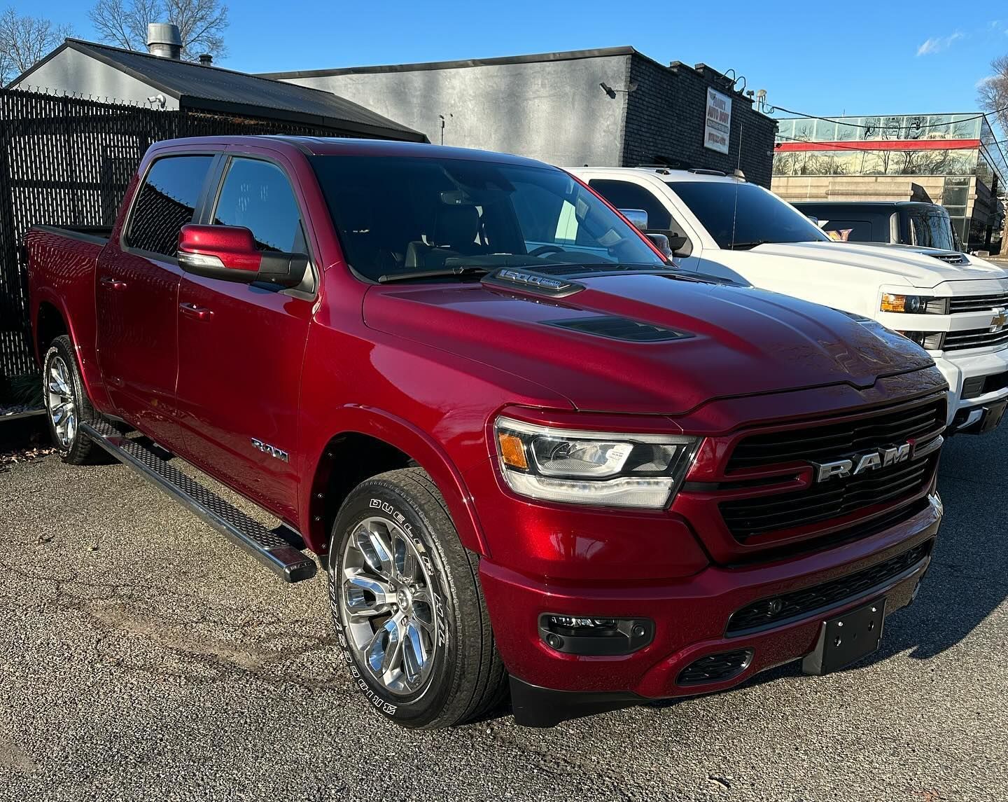 Red Ram truck parked outdoors on a sunny day, chrome accents, near white SUV.
